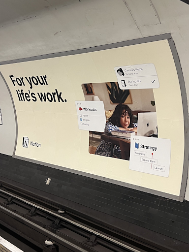 An advert for Notion seen in a tube station that reads 'for your life's work'. It shows 3 UI elements from the application and a photo of a woman sitting on the floor with a laptop.